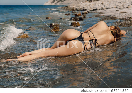 Sexy young woman in bikini posing at stone beach. Attractive model with sporty body Sexy young woman in bikini posing at stone beach. Attractive model with sporty body 67311883