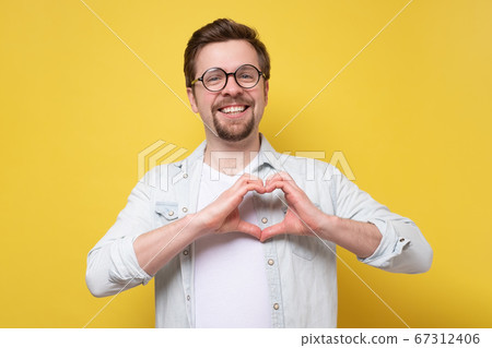 Young caucasian man doing a heart gesture 67312406