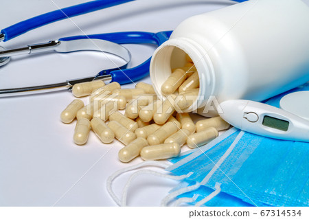 Disposable Medical protective mask with can of pills and thermometer over light grey background Disposable Medical protective mask with can of pills and thermometer over light grey background 67314534