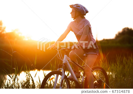 Joyful young woman riding a bicycle at the riverside and meadow promenade 67314878