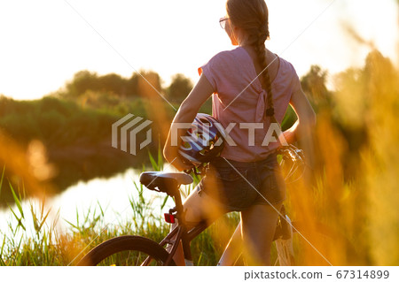 Joyful young woman riding a bicycle at the riverside and meadow promenade Joyful young woman riding a bicycle at the riverside and meadow promenade 67314899