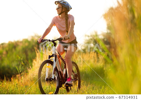 Joyful young woman riding a bicycle at the riverside and meadow promenade 67314931
