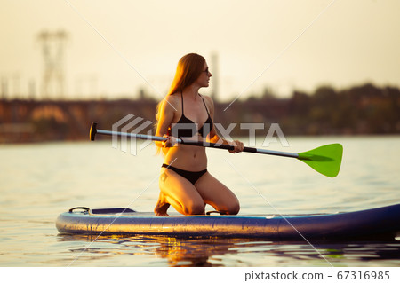 Young attractive woman sitting on paddle board, SUP. Active life, sport, leisure activity concept Young attractive woman sitting on paddle board, SUP. Active life, sport, leisure activity concept 67316985