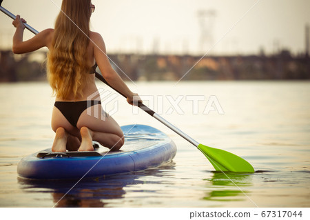 Young attractive woman sitting on paddle board, SUP. Active life, sport, leisure activity concept Young attractive woman sitting on paddle board, SUP. Active life, sport, leisure activity concept 67317044