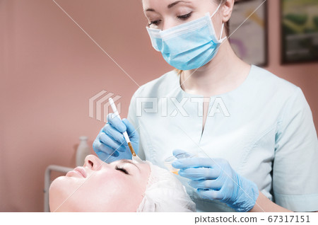 A beautician's office a woman beautician puts a brush rejuvenating mask on the face of an attractive client. Professional cosmetic services A beautician's office a woman beautician puts a brush rejuvenating mask on the face of an attractive client. Professional cosmetic services 67317151