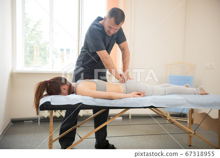 Young woman having osteopathic treatment - the doctor pushing on her butt Young woman having osteopathic treatment - the doctor pushing on her butt 67318955