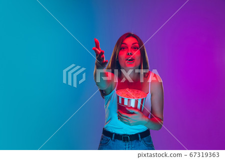 Caucasian young woman's portrait isolated on gradient purple-blue background in neon light, cinema, movie watching 67319363