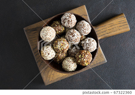 Raw vegetarian energy balls with cashews, hazelnuts, peanut butter and almond in the wooden bowl on the board on the dark background. Homemade, organic food. Flat lay, close up. 67322360