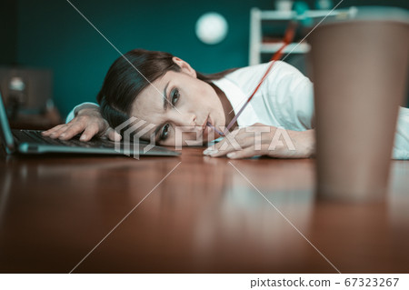 Tired businesswoman drinks coffee resting on office table. Bored crazy girl drinks coffee through long tube lying at workplace. Crisis concept. Tinted image Tired businesswoman drinks coffee resting on office table. Bored crazy girl drinks coffee through long tube lying at workplace. Crisis concept. Tinted image 67323267