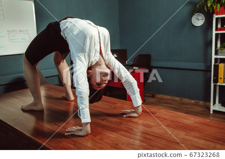 Fitness during work break. Young Caucasian business woman doing bridge exercise at office desk. Recreation concept. Yoga concept. Tinted image Fitness during work break. Young Caucasian business woman doing bridge exercise at office desk. Recreation concept. Yoga concept. Tinted image 67323268