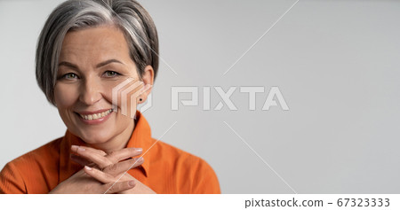 Mature woman broadly smiling with fingers crossed. Happy female model in orange shirt. Close up portrait. Maturity concept. Horizontal template with empty place at right side 67323333