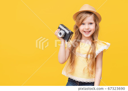 Portrait of a happy child a little blonde girl with long hair on a Colored yellow background with a retro camera in her hands. The concept of rest, travel. Portrait of a happy child a little blonde girl with long hair on a Colored yellow background with a retro camera in her hands. The concept of rest, travel. 67323690