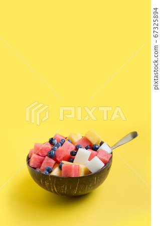 Fruits salad of melon, watermelon in coconut bowl on yellow background. Healthy breakfa Clean eating. Vertical. 67325894