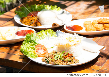 basil stir fry rice with vegetable tomato cucamber salad on white plate and wood table with another food stock photo 67328191