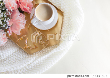 White cup of coffee and decorations on a golden tray in the nordic style. Pink peonies. A white plaid lies on a leather sofa. White cup of coffee and decorations on a golden tray in the nordic style. Pink peonies. A white plaid lies on a leather sofa. 67331305