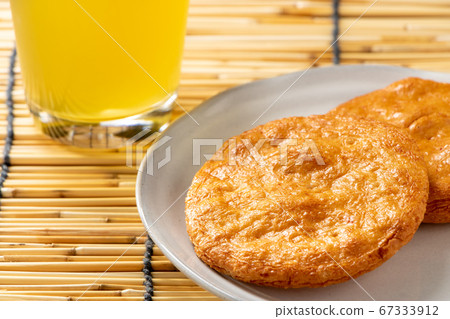Soy sauce rice cracker. In the back of the photo is a glass of cold tea. 67333912