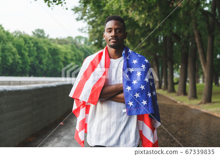 Afro American man with USA flag on his shoulders looking at camera, standing outdoors. Day summer 67339835
