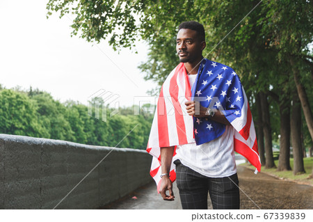 Afro American man with USA flag on his shoulders standing outdoors. Day summer 67339839