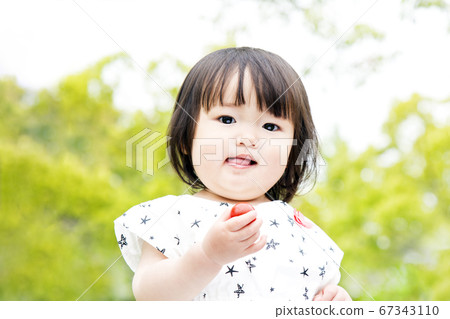 在新鮮的綠樹的背景下吃櫻桃西紅柿的小女孩 67343110