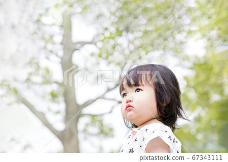 Little girl gazing into the distance against the backdrop of fresh green trees 67343111