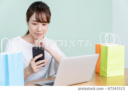 一個年輕的女人,與智能手機和計算機在線購物 一個年輕的女人,與智能手機和計算機在線購物 67343313