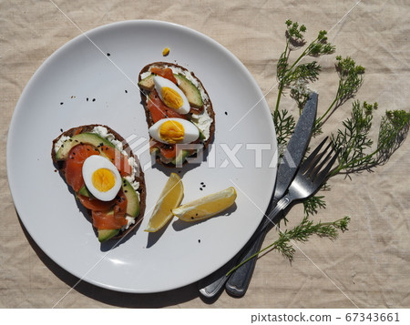 Sandwiches with cheese, fish and an egg in a white plate on a textile background.A sprig of cilantro plants nearby. Flat lay. 67343661