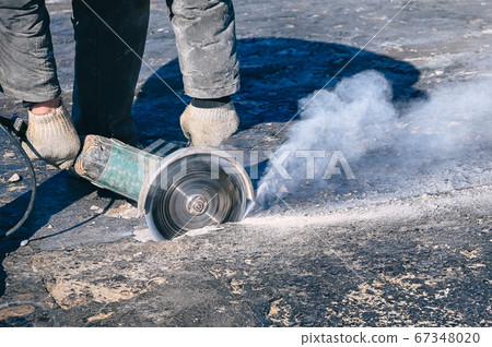 Circular saw cutting reinforced concrete slab during roof repair. Worker hands with with electric angle grinder closeup. Circular saw cutting reinforced concrete slab during roof repair. Worker hands with with electric angle grinder closeup. 67348020
