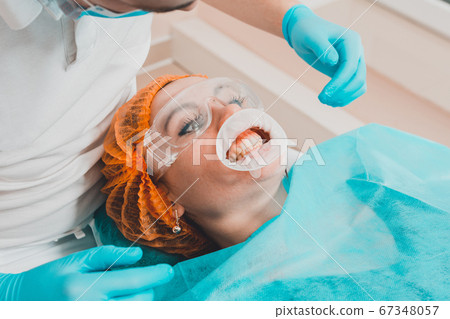 A young female dentist pulls a mouth extender at a A young female dentist pulls a mouth extender at a 67348057