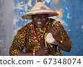 African man in traditional clothes and fulani hat playing on talking drum 67348074