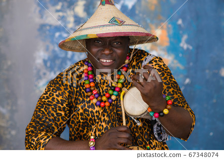 African man in traditional clothes and fulani hat playing on talking drum African man in traditional clothes and fulani hat playing on talking drum 67348074