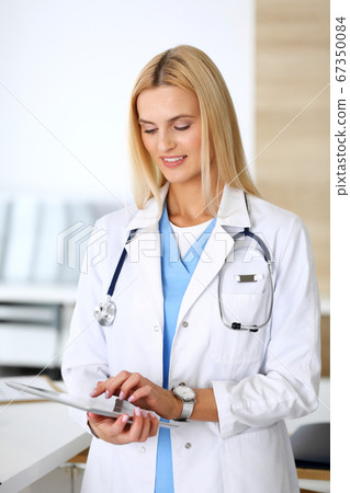 Doctor woman at work in hospital excited and happy of her profession. Blonde physician controls medication history records and exam results while using tablet computer. Medicine and healthcare concept Doctor woman at work in hospital excited and happy of her profession. Blonde physician controls medication history records and exam results while using tablet computer. Medicine and healthcare concept 67350084