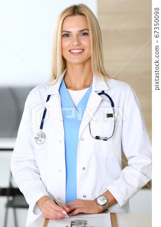 Doctor woman at work in hospital excited and happy of her profession. Blonde physician controls medication history records and exam results while using clipboard. Medicine and healthcare concept Doctor woman at work in hospital excited and happy of her profession. Blonde physician controls medication history records and exam results while using clipboard. Medicine and healthcare concept 67350098