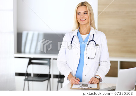 Doctor woman at work in hospital excited and happy of her profession. Blonde physician controls medication history records and exam results. Medicine and healthcare concept 67350108