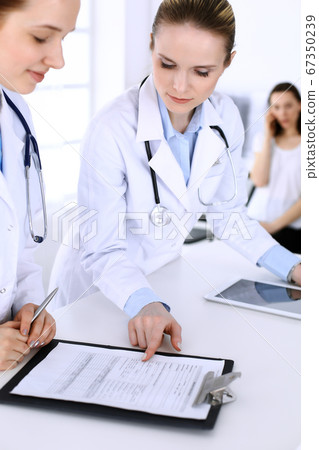 Group of doctors at work in hospital with patient in a queue at the background. Physician filling up medical documents or prescription while standing at reception desk. Data in medicine and health 67350239