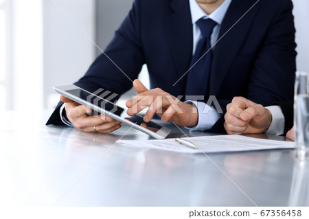 Business people using tablet computer while working together at the desk in modern office. Unknown businessman or male entrepreneur with colleague at workplace. Teamwork and partnership concept Business people using tablet computer while working together at the desk in modern office. Unknown businessman or male entrepreneur with colleague at workplace. Teamwork and partnership concept 67356458