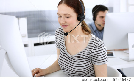 Group of operators at work. Call center. Focus on beautiful woman receptionist in headset at customer service. Business concept and casual striped clothing style 67356487