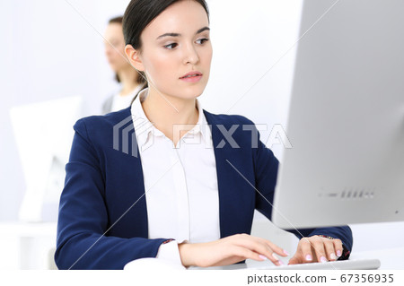 Business woman working with computer in office, female colleague at background. Headshot of Lawyer or accountant at work while sitting at the desk Business woman working with computer in office, female colleague at background. Headshot of Lawyer or accountant at work while sitting at the desk 67356935