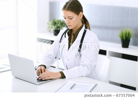 Doctor typing on laptop computer while sitting at the desk in hospital office. Physician woman at work. Data in medicine and healthcare Doctor typing on laptop computer while sitting at the desk in hospital office. Physician woman at work. Data in medicine and healthcare 67357004