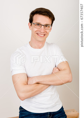 Young worker wearing jeans and a white tshirt sits on a white board and smiles looking straight at the camera. 67357407