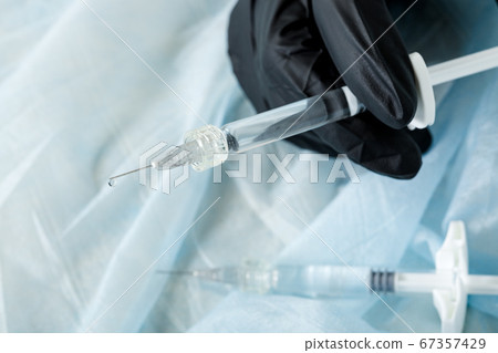 Gloved hand holding a syringe with cosmetic injection on a light background. Plastic and aesthetic surgery. 67357429