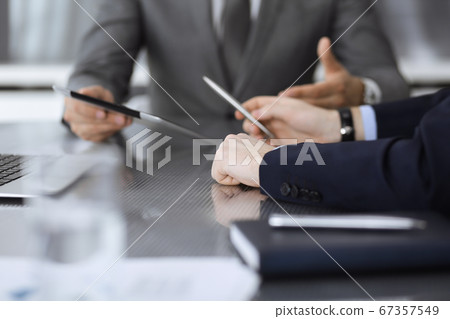 Unknown businessman using tablet computer and working together with his colleague while sits at the glass desk in modern office. Teamwork and partnership concept 67357549