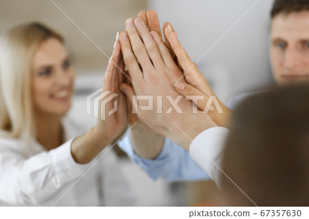 Group of business people joining hands or giving five to each other after meeting or negotiation in modern office. Colleagues showing teamwork, cooperation and partnership in corporate occupation 67357630