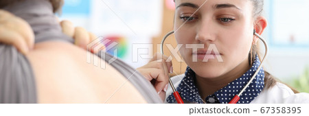 Woman therapist in clinic listens to lungs man 67358395