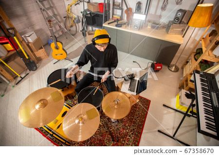 Young drummer with headphones beating drum and cymbal during rehearsal Young drummer with headphones beating drum and cymbal during rehearsal 67358670