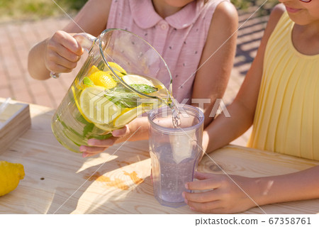 Little girl pouring fresh cool homemade lemonade into plastic glass by stall 67358761