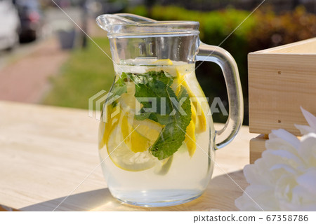 Glass jug with fresh cool homemade lemonade standing on wooden market stall Glass jug with fresh cool homemade lemonade standing on wooden market stall 67358786