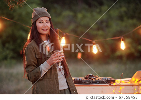 Happy Asian girl with long hair holding drink while standing against lights 67359455