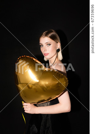 Blond girl holding heart shaped balloon of golden color at valentine party 67359696