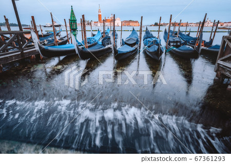 Gondolas floating in the Grand Canal in evening warm light, San Giorgio Maggiore church in background. Long exposure 67361293