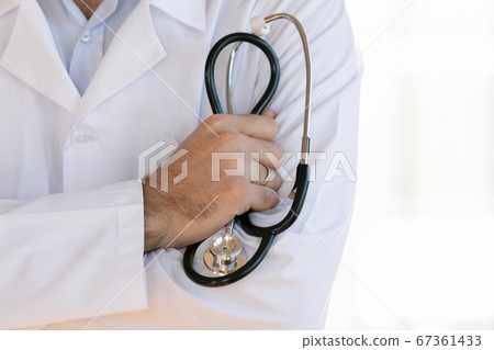 Close up male doctor wearing white uniform holding stethoscope Close up male doctor wearing white uniform holding stethoscope 67361433